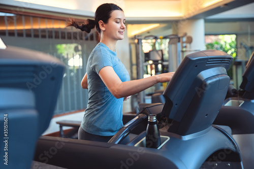Attractive young sports woman is working out in gym doing cardio training running on treadmill in sport club
