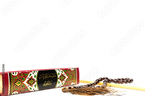 A picture of Quran, tasbeeh and pointer on isolated copyspace white background. Large Arabic word mention the Holy Quran is with variance recitation and correct pronounciations method.