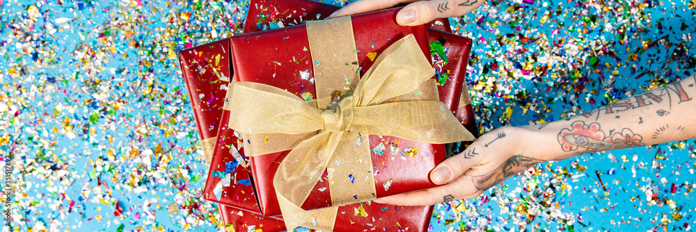 Fotografie Tattooed hand holding red gift boxes with confetti
