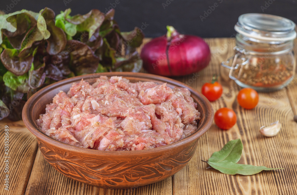 Raw minced pork in a plate and fresh vegetables on a table close-up.