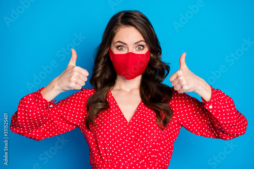 Closeup photo of pretty lady raise thumb fingers up not take off face mask responsible citizen wear dotted red blouse dress protective facial mask isolated blue color background photo