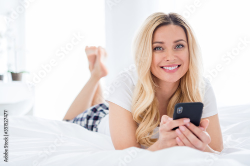 Closeup photo of cheerful beautiful house wife lady hold telephone writing blog post lying cosy bed freelancer quarantine white linen warm sunny morning stay home wear pajama room indoors