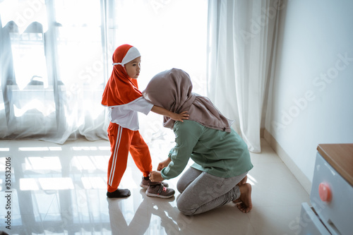 muslim mother help daughter to put on shoes before school