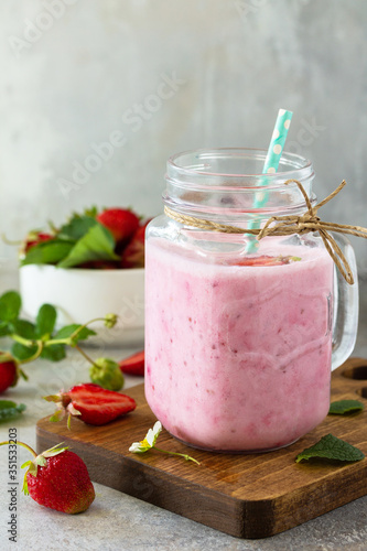 Natural detox, fruit dessert, healthy dieting concept. Strawberry fruit Yogurt smoothie or milk shake in glass jar on a light stone or slate table. Copy space.