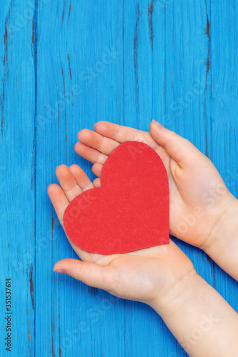 Top view of hands of child holding red heart on blue background  Donation concept.