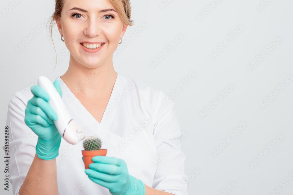 Cosmetologist is shaving green cactus in a brown pot with electric epilator wearing gloves smiling on white background. Concept of depilation, epilation and removal hair. Cosmetologist is shaving green cactus in a brown pot with electric epilator wearing gloves smiling on white background. Concept of depilation, epilation and removal hair.