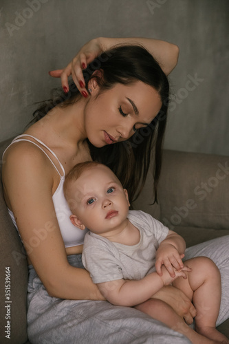 Beautiful portrait of mother and child in dark tones. Stylish prety brunet young woman with baby boy toddler playing smiling hug in studio. Love and tender feelings