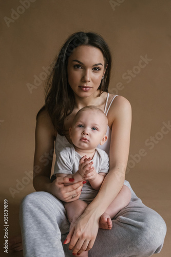 Beautiful portrait of mother and child in dark tones. Stylish prety brunet young woman with baby boy toddler playing smiling hug in studio. Love and tender feelings