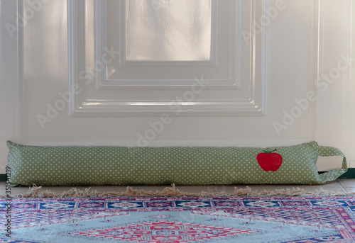 green draught excluder against a white door, to reduce the flow of air from outside entering the house