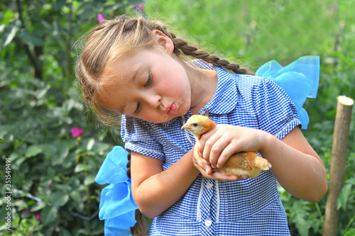 happy little smiling girl holding her hen outside the countryside house in a sunny summer day. Concept: love for animals and nature.Happy childrens day.sisters day