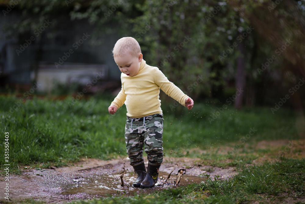 a little boy in rubber boots running in the puddle a little boy in rubber boots running in the puddle