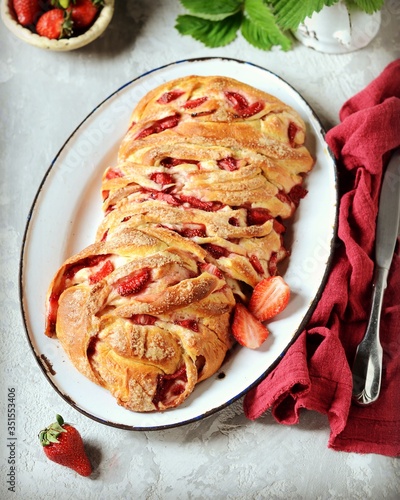 Yeast babka with strawberries and sugar in a dish on a gray background