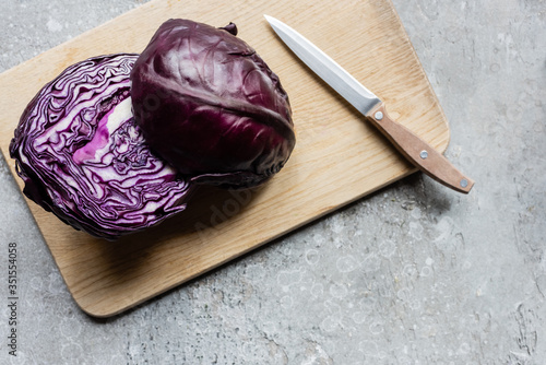 top view of red cabbage on wooden cutting board with knife on grey concrete surface photo