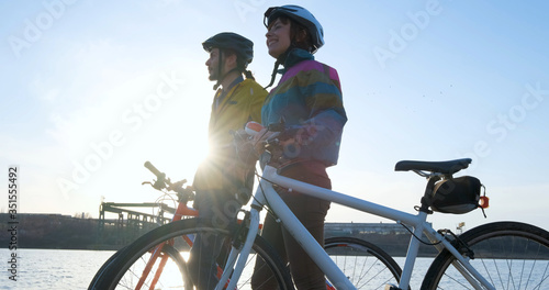 Fototapeta Naklejka Na Ścianę i Meble -  Couple of male and female ride on bicycles near river during sunset	