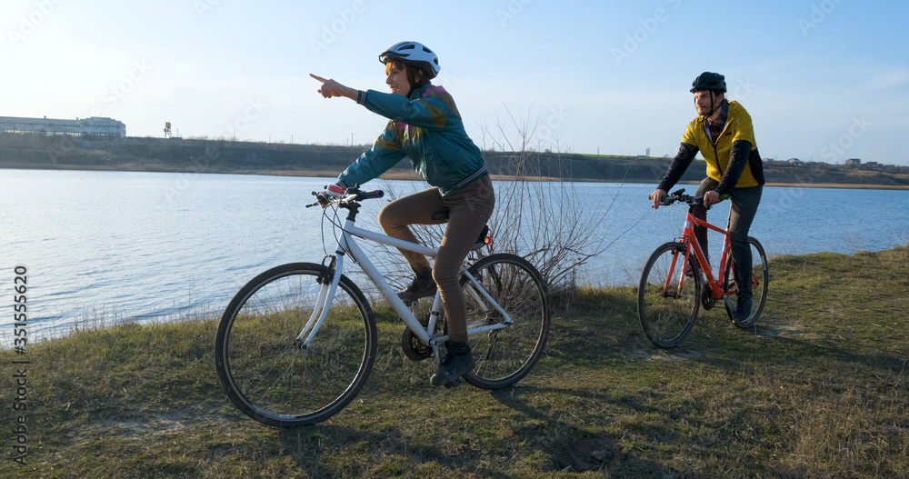 Fototapeta premium Couple of male and female ride on bicycles near river during sunset 