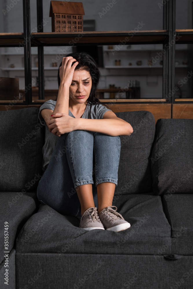 Obraz premium upset woman with bruise on face sitting on sofa, domestic violence concept