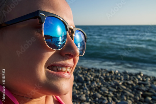 A girl with a removable orthodontic appliance and in sunglasses sits on the seashore. Concept of pediatric dentistry, correcting the bite.