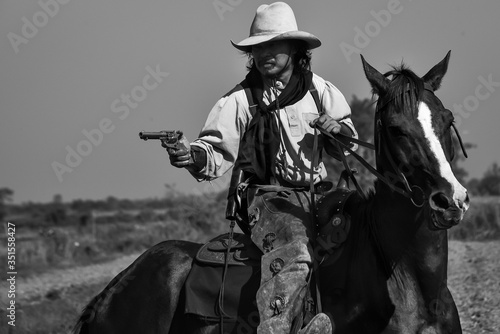 Vintage image of a cowboy man riding a horse and a gun in his hand © Surachai