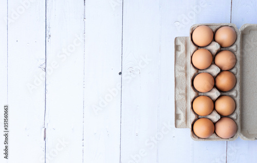 Top view chicken eggs in carton box on white wooden table.