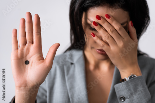 selective focus of sad businesswoman showing hand with black dot on palm and covering eyes isolated on white, domestic violence concept