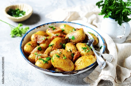 Young baked potato with bacon, spices and herbs in a baking dish on a gray background, still life