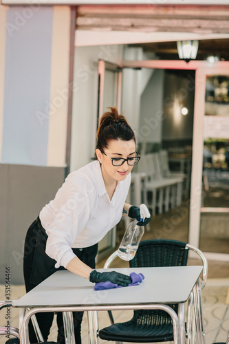 Waitress disinfecting restaurant chairs and tables before the next customers sit down. New normal