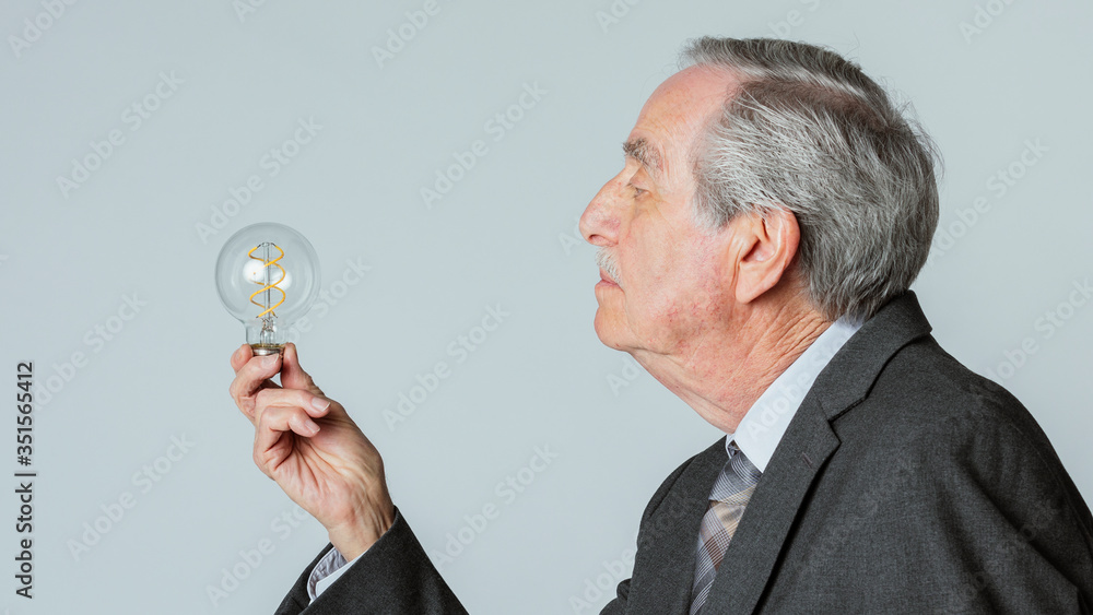 Senior businessman holding a light bulb in a profile shot Senior businessman holding a light bulb in a profile shot