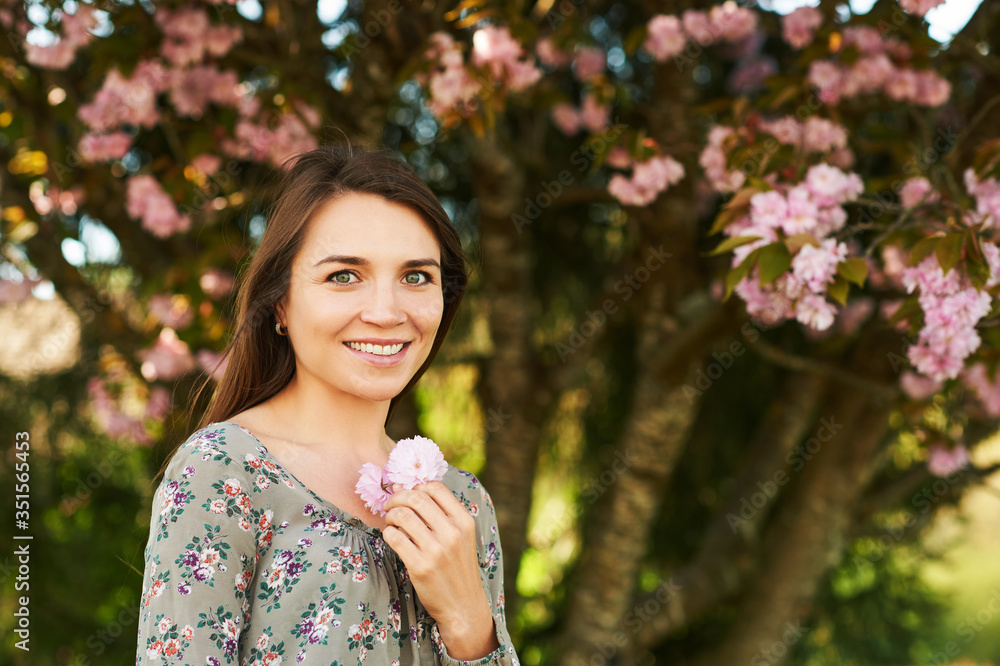 Outdoor spring portrait of pretty young woman with brown hair posing under pink blossoming tree Outdoor spring portrait of pretty young woman with brown hair posing under pink blossoming tree