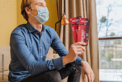 young man in medical mask holding night party tickets, end of quarantine concept