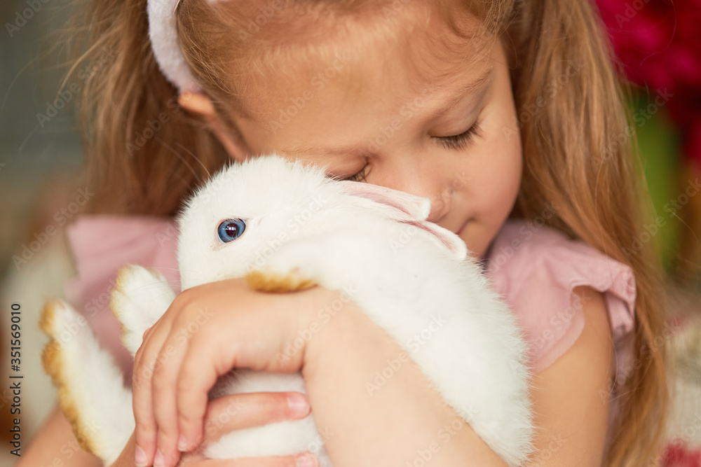 Pet care. Little child girl hugs a cute white rabbit at home. Pet care. Little child girl hugs a cute white rabbit at home.