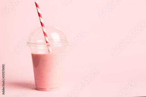 Glass of fresh strawberry milkshake, smoothie and fresh strawberries on pink, white and wooden background. Healthy food and drink concept.