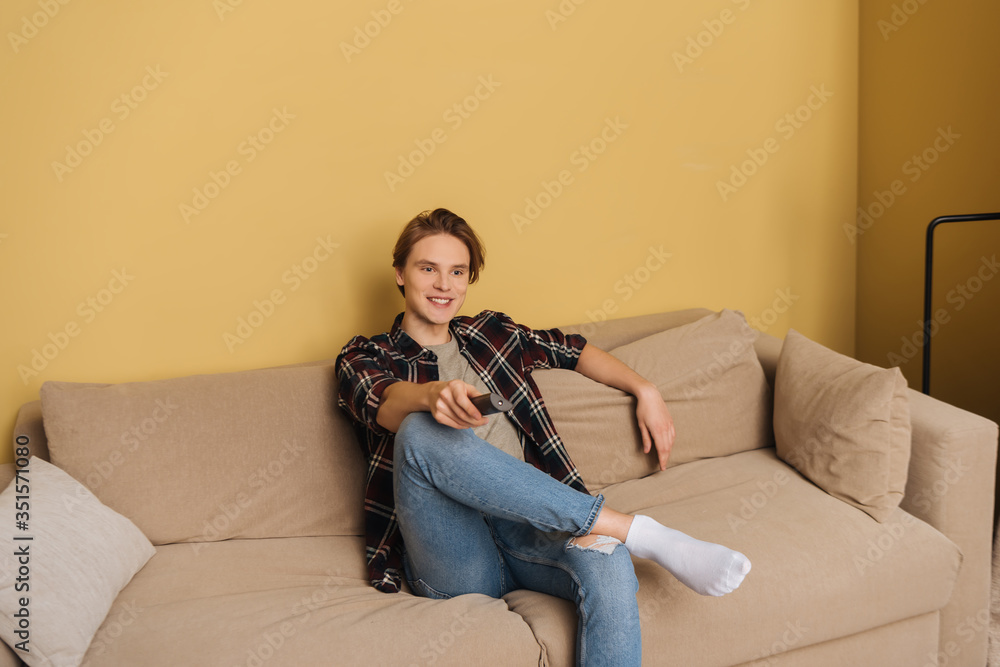 Obraz premium happy man holding remote controller and sitting on sofa, end of quarantine concept