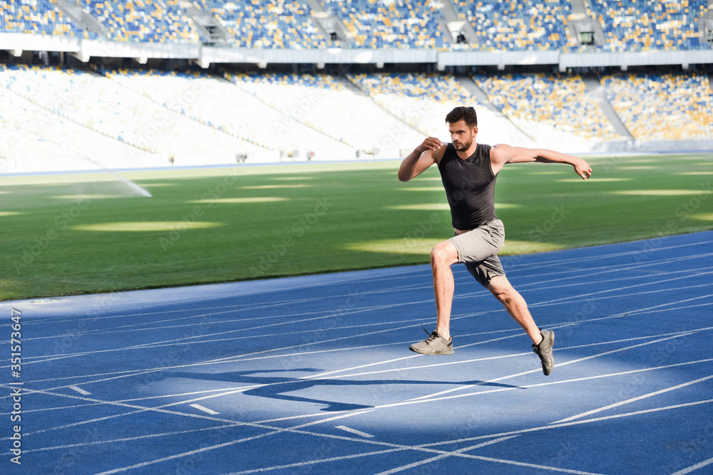 fast handsome runner exercising on running track at stadium