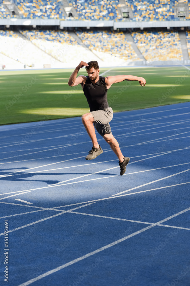 fast handsome runner exercising on running track at stadium