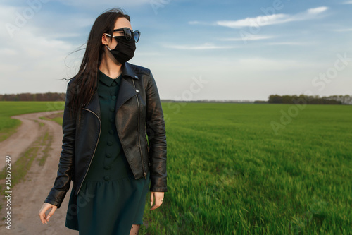 A girl in a medical mask runs or walks on a green field. Quarantine spring summer. coronavirus. COVID 19. Flu virus, colds photo