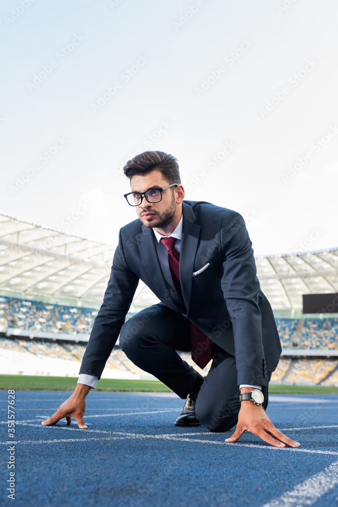 young businessman in suit in start position on running track at stadium young businessman in suit in start position on running track at stadium