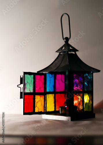 lantern in the form of a house with colorful bright Windows with a burning candle on a white background