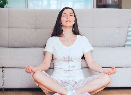 A young woman meditating in the living room while listening to music.