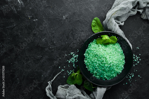 Green sea salt in a bowl. On a black stone background. Spa treatments. Top view. Free space for your text.