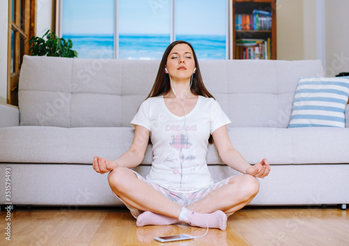A young woman meditating in the living room while listening to music.