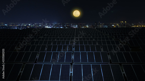 Solar panels at night with full moon and city background.