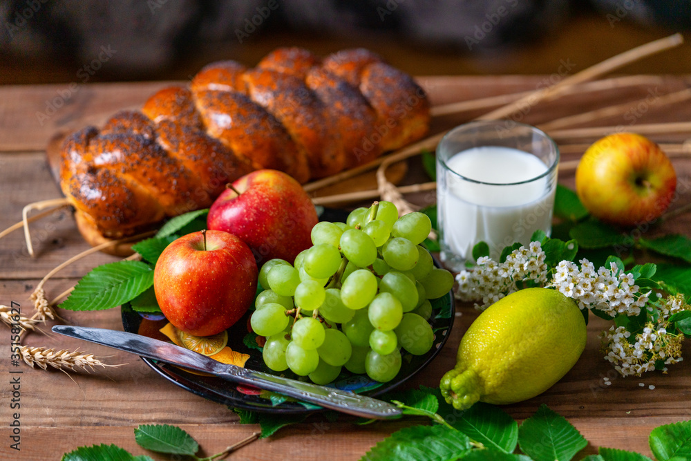 Wicker bun, lemon, apples, green grapes, wheat and a glass with milk on a wooden table. Jewish holiday Shavuot. Wicker bun, lemon, apples, green grapes, wheat and a glass with milk on a wooden table. Jewish holiday Shavuot.
