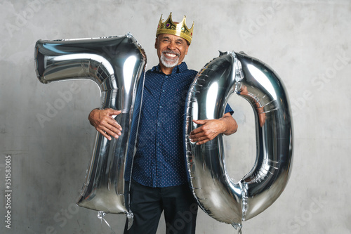 Cheerful senior man holding silver balloons for his 70th birthday celebration photo