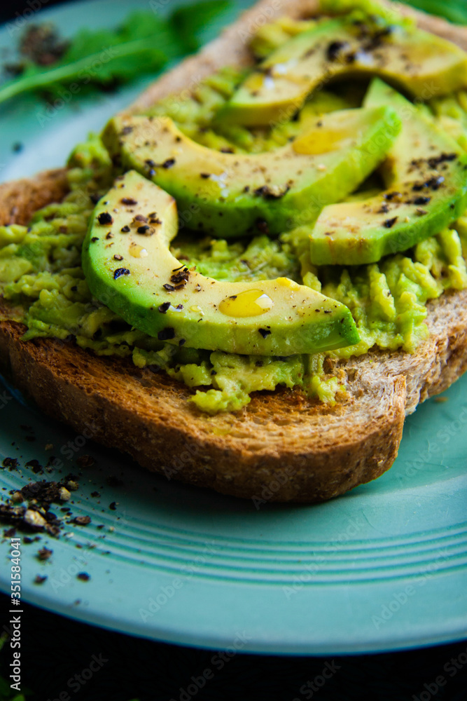 Close up of avocado smash on wholemeal toast, sprinkled with black pepper, and a splash of olive oil, vegan healthy meal, home cooked and family friendly. Bright colours, shallow depth of field.