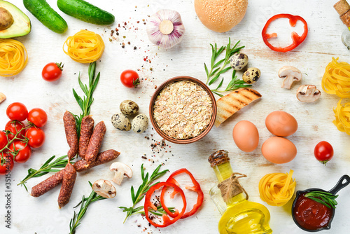 White wooden food background: tomatoes, pasta, spices, vegetables and sausages. Top view.