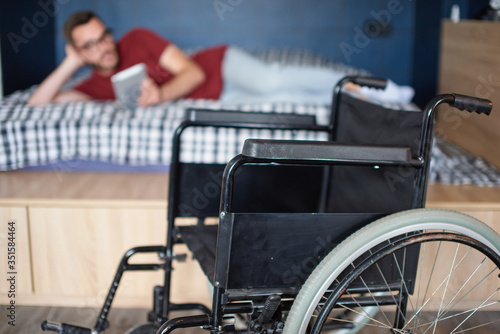 Man reading in bed, wheelchair in front