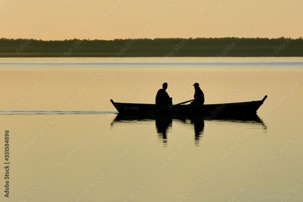 Silhouette of a boat with fishermen on a lake in the evening