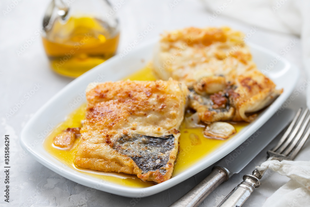 fried cofish with garlic and olive oil on white dish on ceramic background fried cofish with garlic and olive oil on white dish on ceramic background