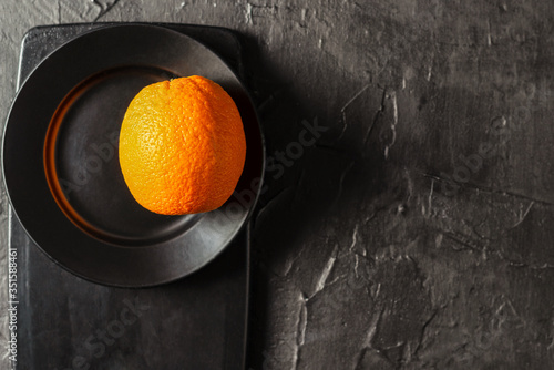 fresh whole orange on a smooth black plate and cutting black Board and on a textured black background