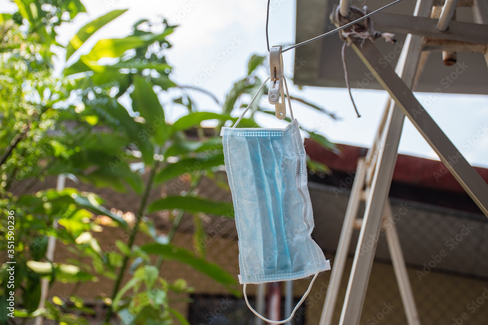 Reused surgical mask is hanging with hanger by clip to dry from sun light for sterilize outside.